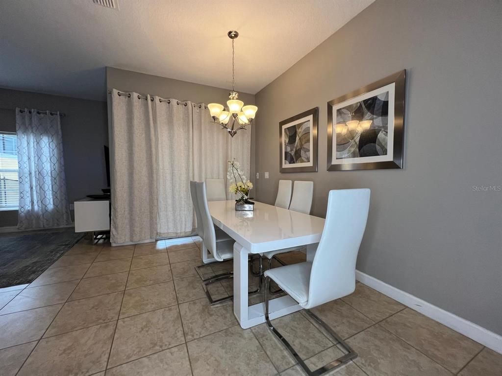 A dining room features a white table, six white chairs, and a modern chandelier — 2937 BANANA PALM DRIVE, KISSIMMEE, FL