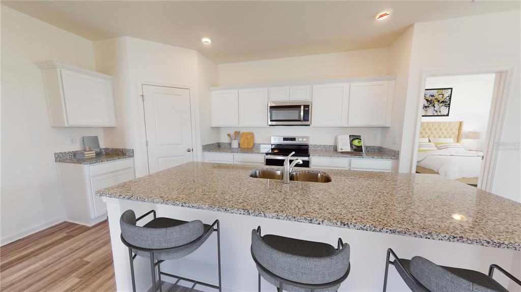 A kitchen features a granite island with bar stools, white cabinets, and stainless steel appliances — 5555 BELDI DRIVE, POLK CITY, FL