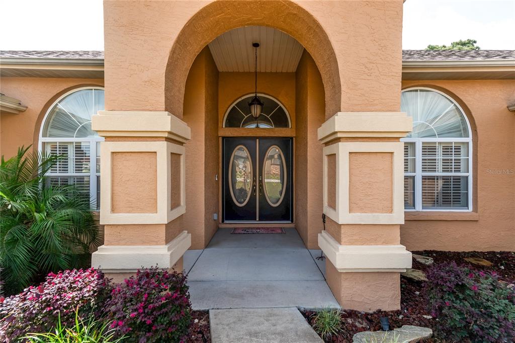 The exterior entrance features a covered porch with an arched ceiling and double front doors — 10411 SW 52ND COURT, OCALA, FL
