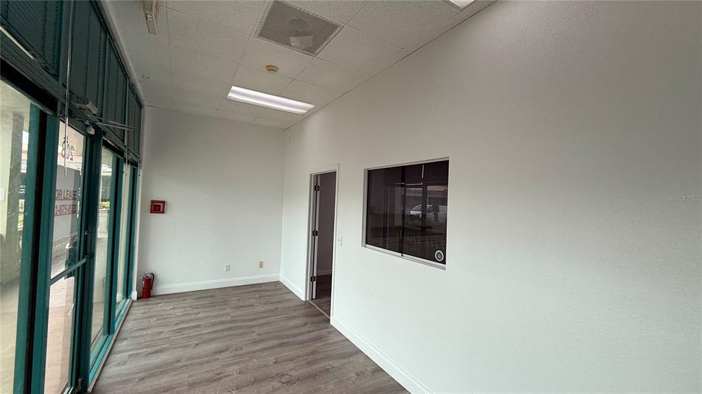 An empty commercial office space features white walls, wood-look flooring, a window, and a doorway — 20101 PEACHLAND BOULEVARD, PORT CHARLOTTE, FL