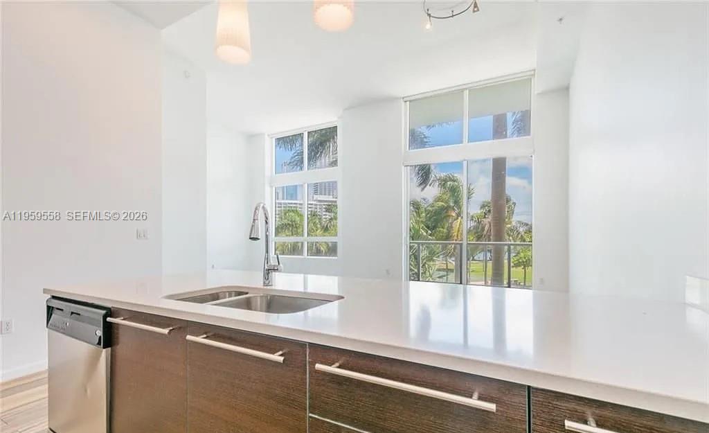 A modern kitchen features dark wood cabinets, white countertops, and large windows with palm trees — 1900 N Bayshore Dr # 506, Miami FL 33132, MIAMI, FL