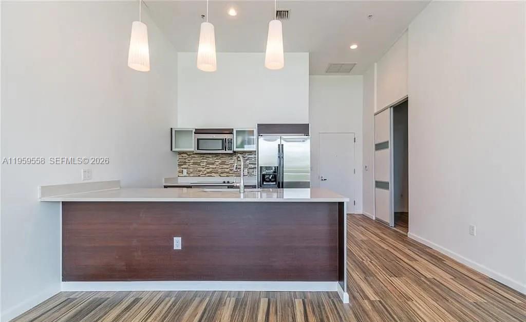 A modern kitchen features a dark wood island, white countertops, and stainless steel appliances — 1900 N Bayshore Dr # 506, Miami FL 33132, MIAMI, FL