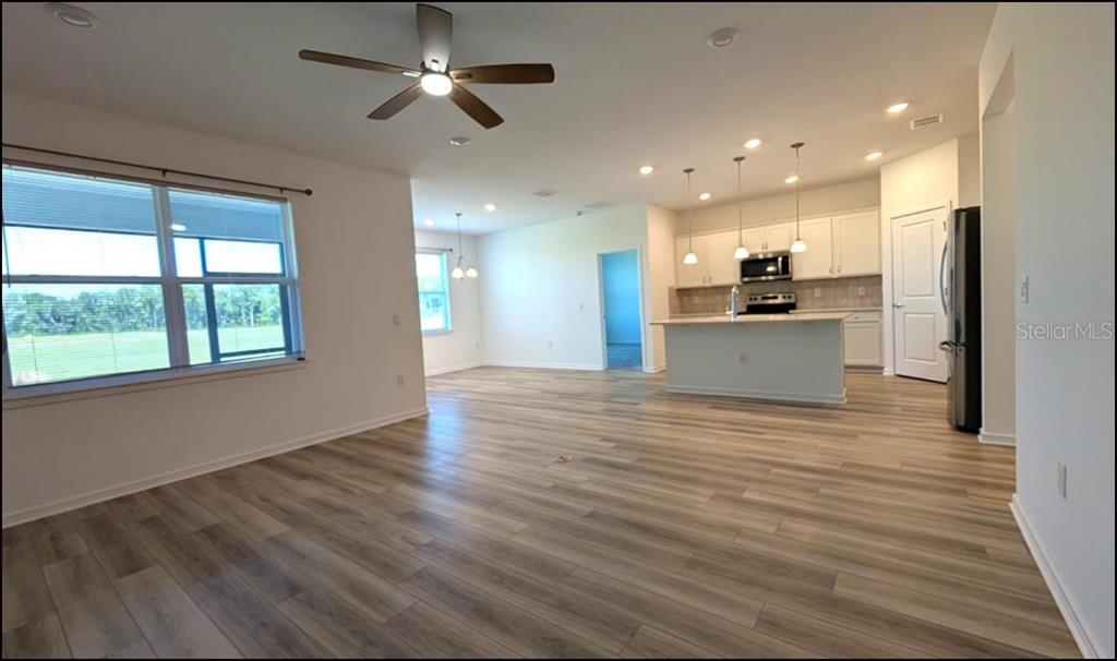 An empty living room features light wood-look flooring, white walls, a ceiling fan, and windows — 8479 SW 52ND LANE ROAD, OCALA, FL