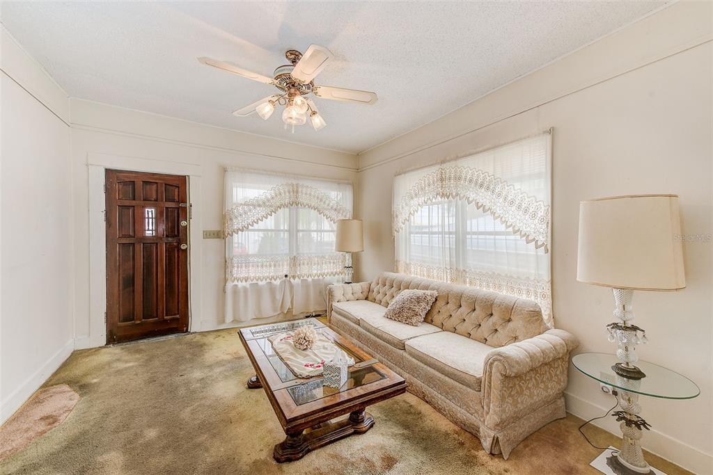 A living room features a tufted sofa, a coffee table, and worn wall-to-wall carpeting — 632 CROSS STREET, TARPON SPRINGS, FL