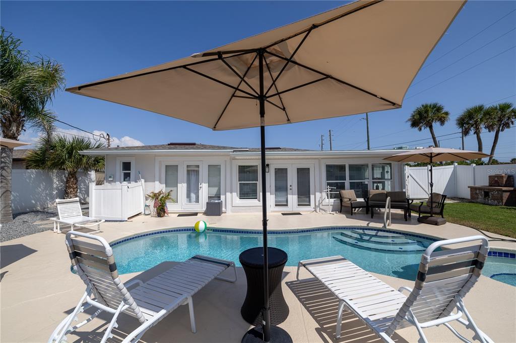 A backyard swimming pool with lounge chairs and umbrellas sits in front of a house — 813 E 6TH AVENUE, NEW SMYRNA BEACH, FL