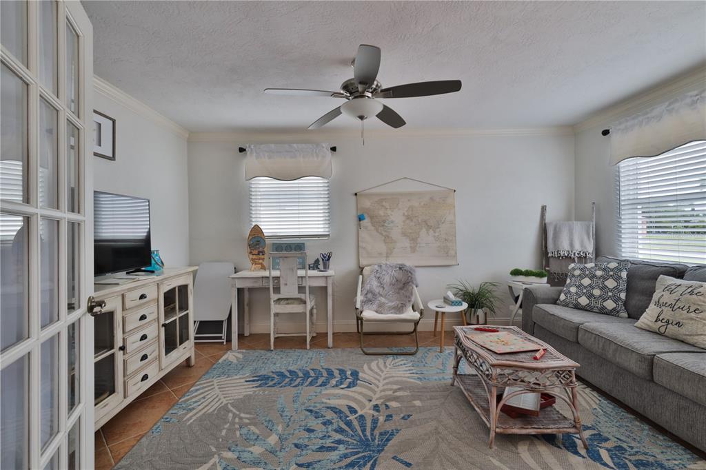 A living room features a gray sofa, a patterned rug, a desk, and a ceiling fan — 813 E 6TH AVENUE, NEW SMYRNA BEACH, FL