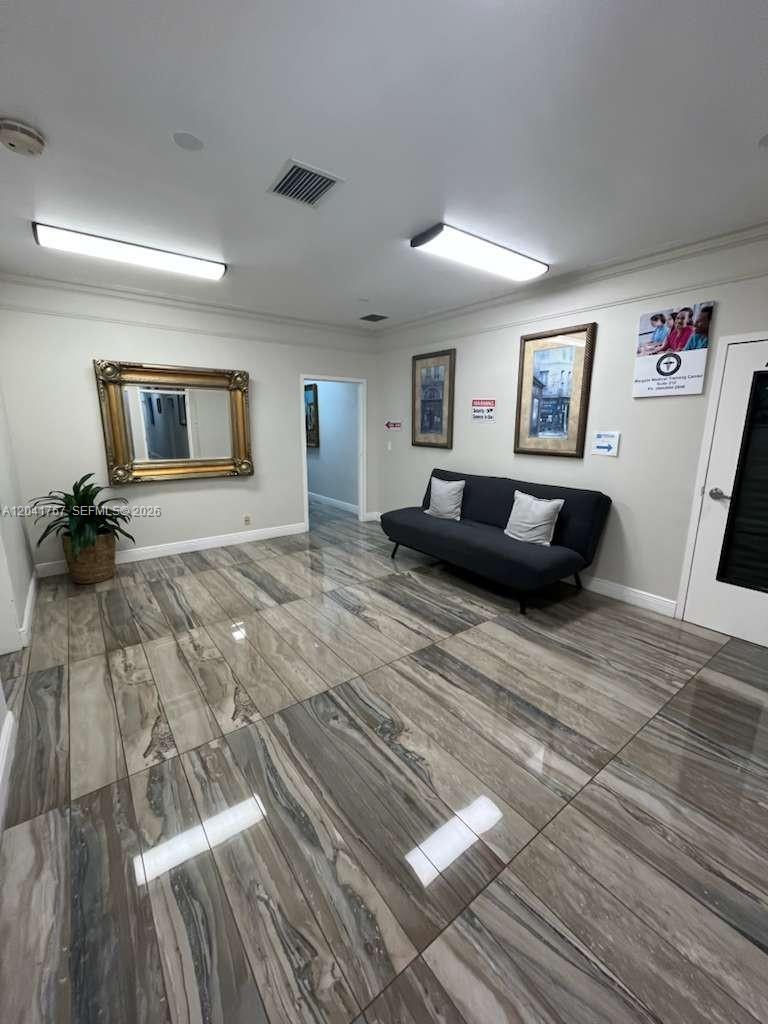 A waiting room features a dark sofa, two framed pictures, a gold-framed mirror, and tiled flooring — 6101 W Atlantic Blvd # 205, Margate FL 33063, MARGATE, FL