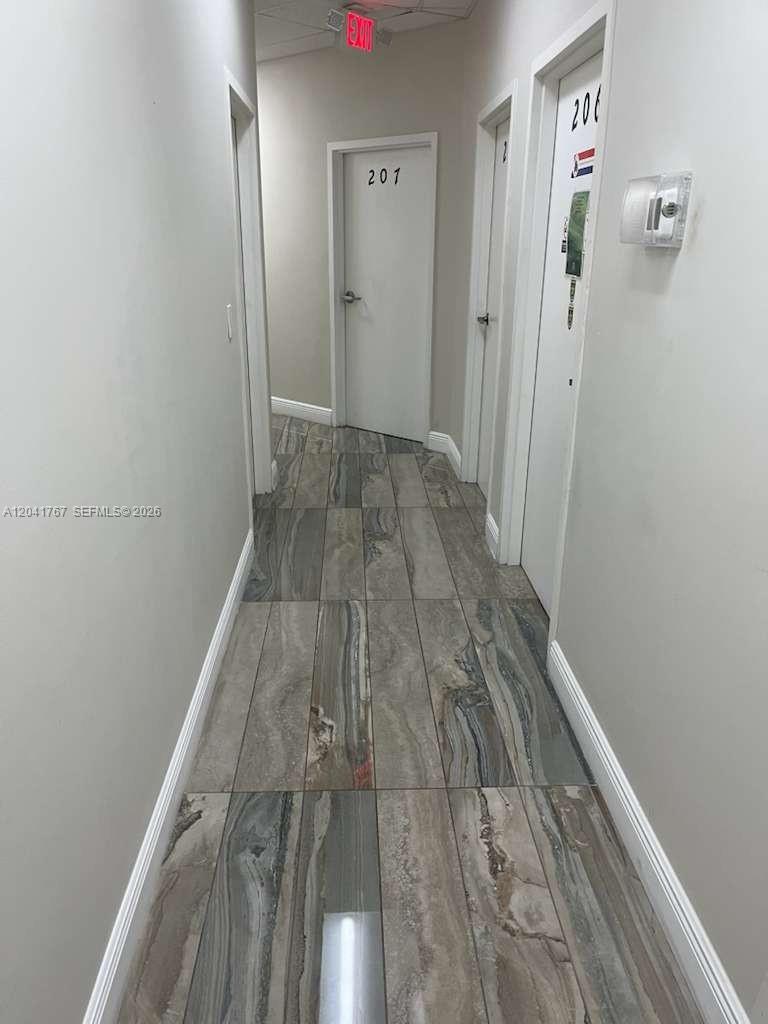 A narrow hallway features light gray walls, white doors, and wood-look tile flooring — 6101 W Atlantic Blvd # 205, Margate FL 33063, MARGATE, FL