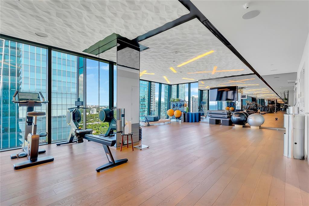 A modern gym features floor-to-ceiling windows, wooden flooring, and a textured white ceiling — 1451 Brickell Avenue # 1202, Miami FL 33131, MIAMI, FL