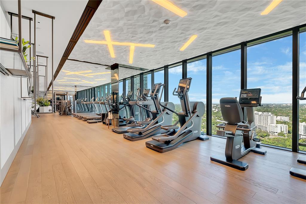 A modern gym features rows of exercise equipment, wood flooring, and floor-to-ceiling windows — 1451 Brickell Avenue # 1202, Miami FL 33131, MIAMI, FL