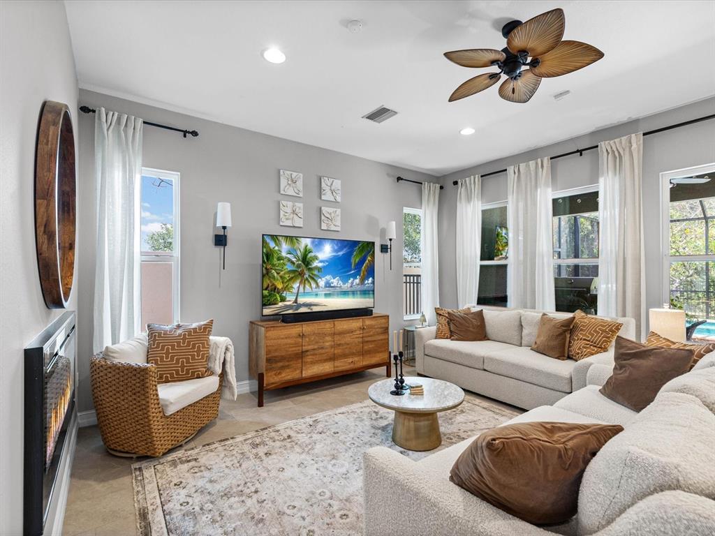 A living room features a television on a wooden console, a sofa, and wicker chair — 3719 WICKET FIELD ROAD, LUTZ, FL