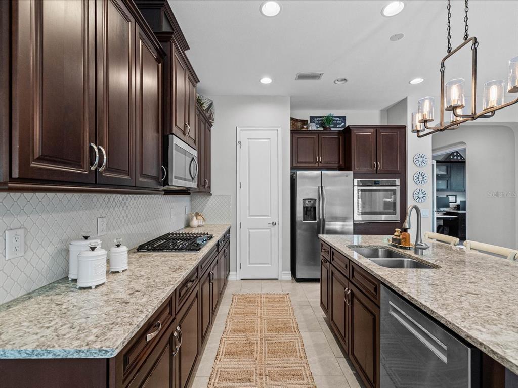 A kitchen features dark wood cabinets, granite countertops, stainless steel appliances, and a central island — 3719 WICKET FIELD ROAD, LUTZ, FL