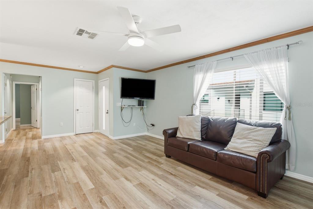 A living room features light wood-look flooring, a brown leather sofa, and a wall-mounted television — 511 MISTLETOE COURT UNIT C, SAFETY HARBOR, FL
