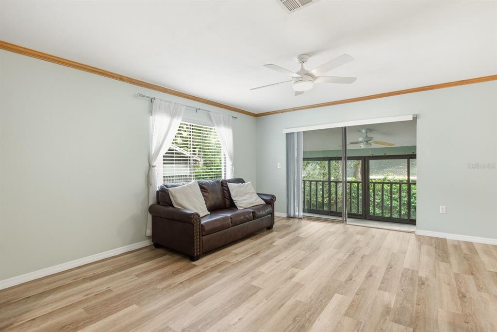 A living room features light green walls, wood-look flooring, a brown sofa, and sliding doors — 511 MISTLETOE COURT UNIT C, SAFETY HARBOR, FL