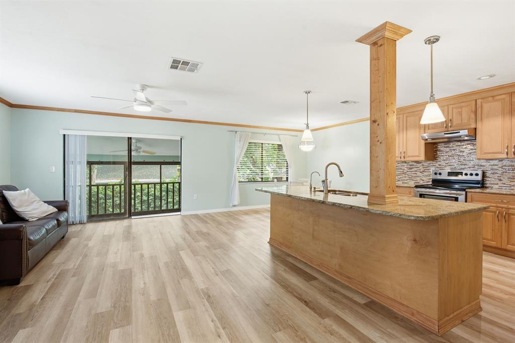 An open-concept kitchen and living area features light wood flooring, a granite island, and cabinetry — 511 MISTLETOE COURT UNIT C, SAFETY HARBOR, FL
