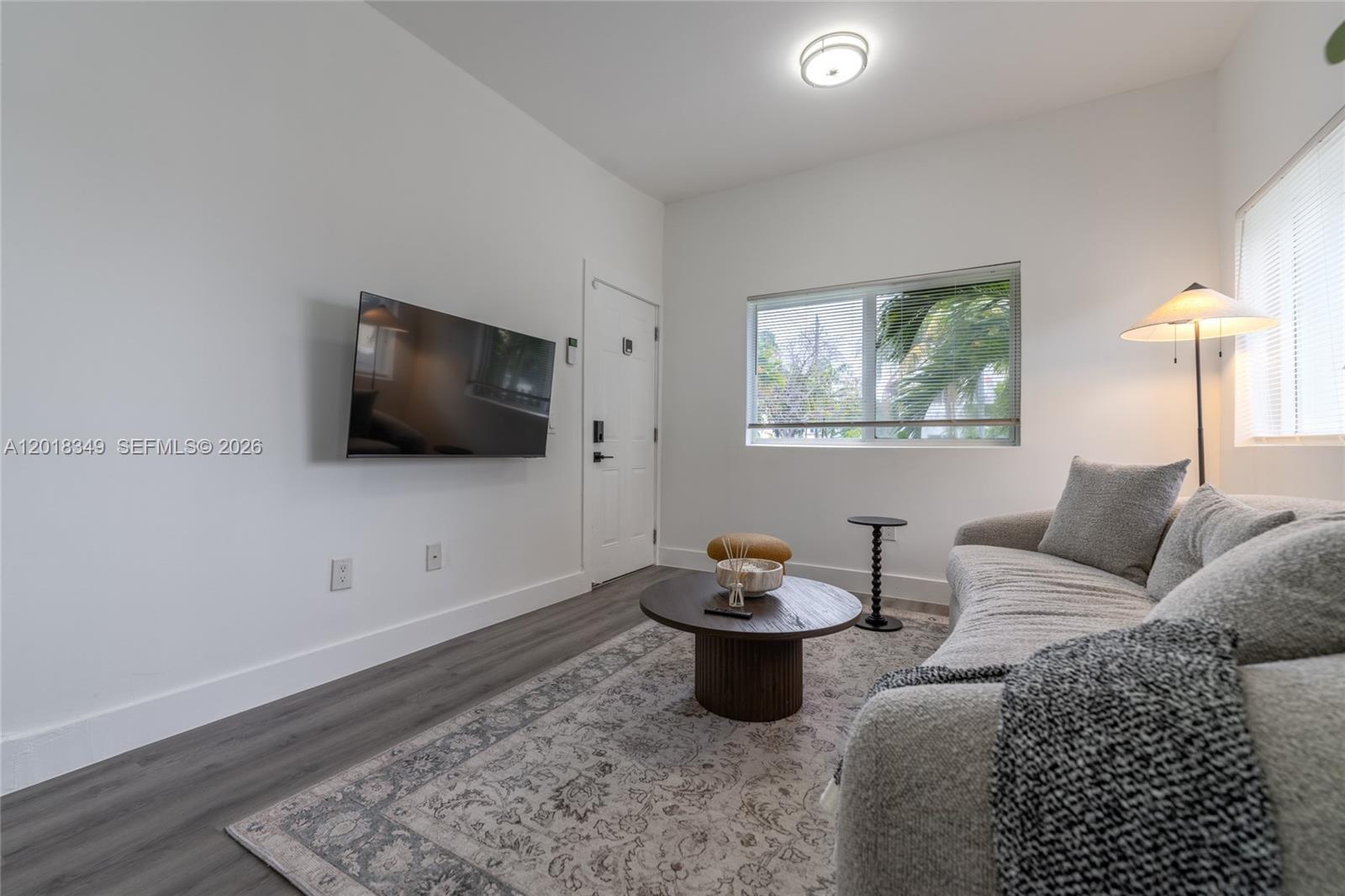 A living room features a wall-mounted television, a gray sofa, and a round coffee table — 44 NW 10th Ave # 2, Miami FL 33128, MIAMI, FL