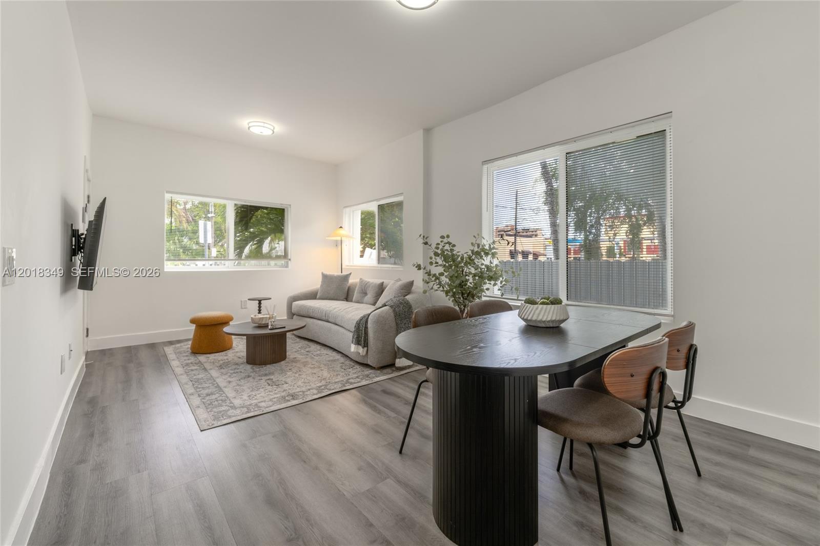 A living and dining room features gray wood-look flooring, white walls, and two large windows — 44 NW 10th Ave # 2, Miami FL 33128, MIAMI, FL