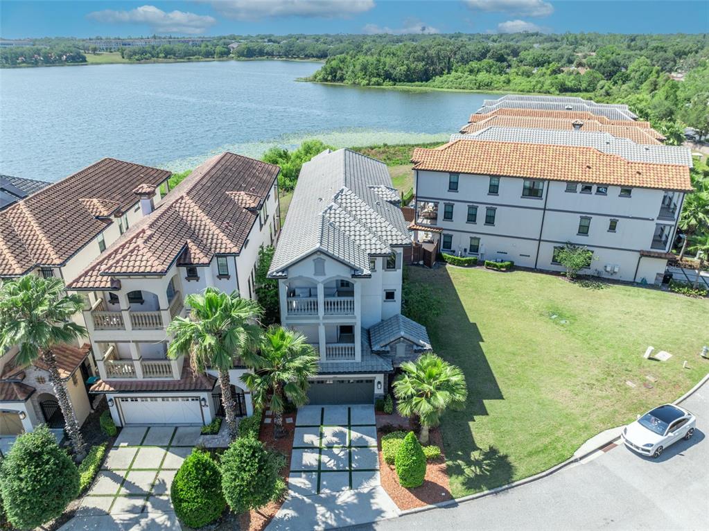 An aerial view shows three multi-story houses near a lake with a paved driveway below — 7613 TOSCANA BOULEVARD, ORLANDO, FL