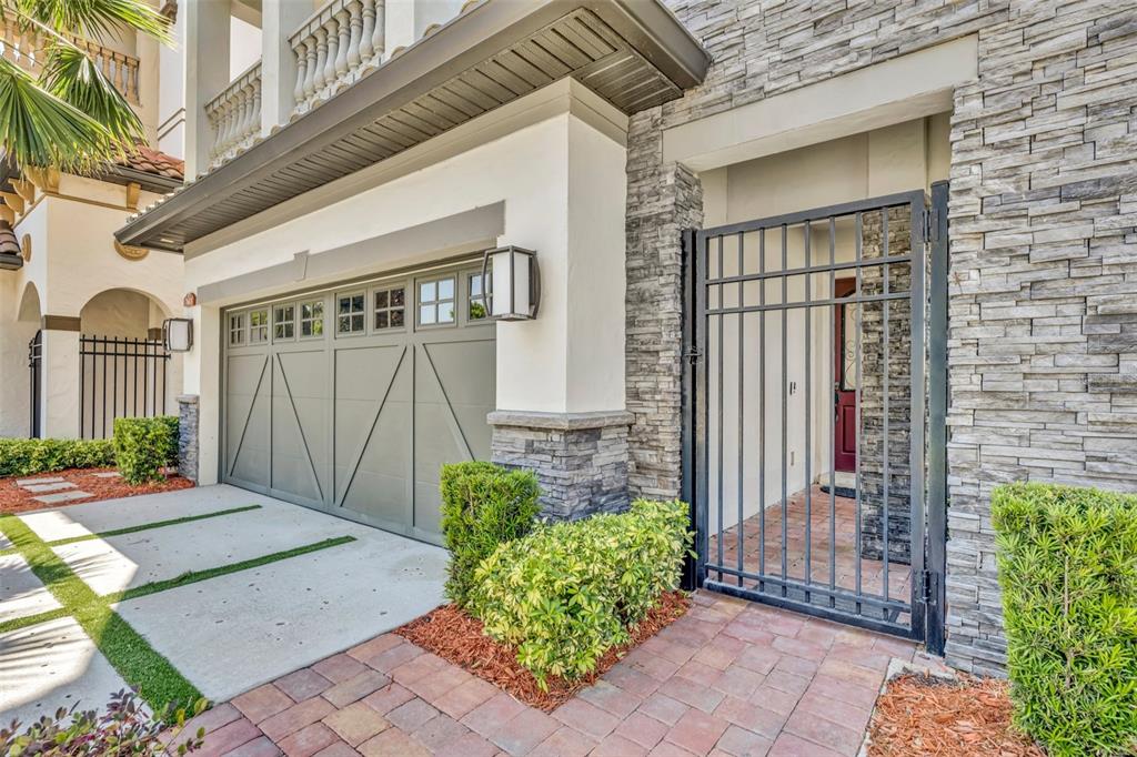 A house exterior features a gray garage door, a stone facade, and a metal gate — 7613 TOSCANA BOULEVARD, ORLANDO, FL