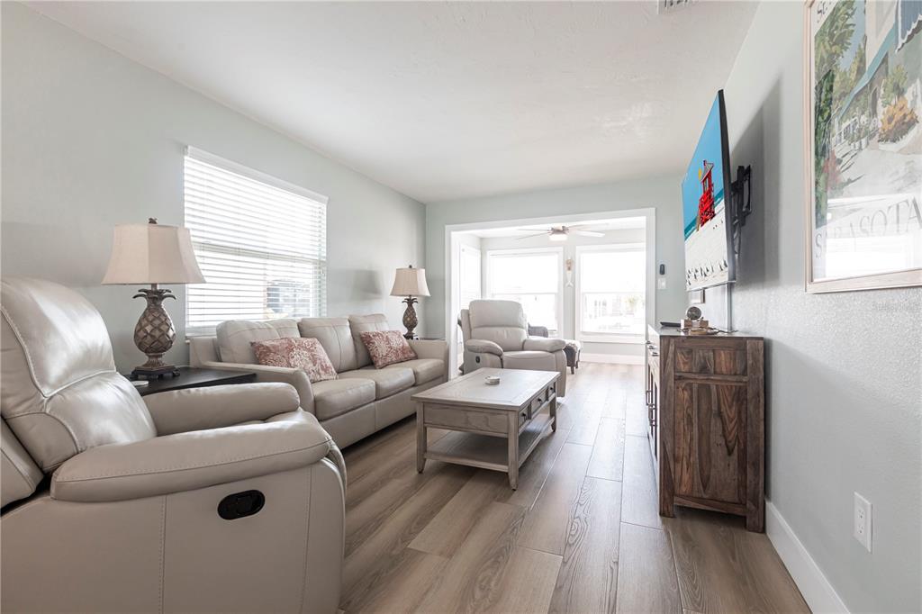 A living room features light-colored walls, wood-look flooring, a sofa, recliners, and a television — 6020 MIDNIGHT PASS ROAD UNIT 35, SARASOTA, FL