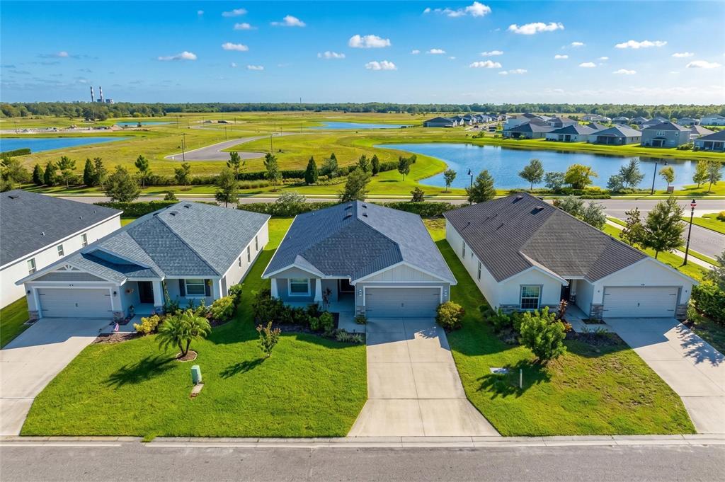 An aerial view shows three suburban houses with driveways facing a street and pond — 6708 162ND PLACE E, PARRISH, FL