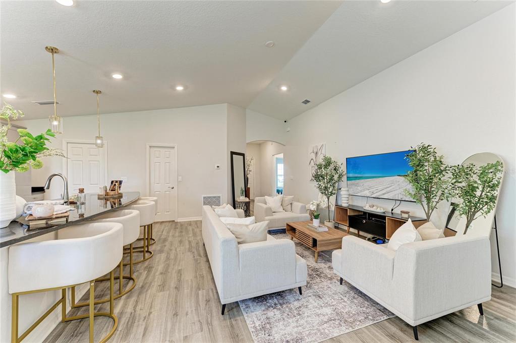 A modern open-concept living room features a kitchen island, white sofas, and wood flooring — 6708 162ND PLACE E, PARRISH, FL