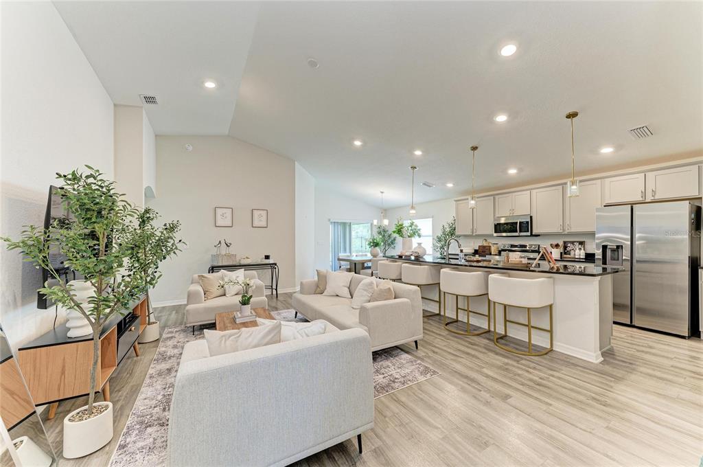 An open-concept living room and kitchen with light wood floors, white cabinetry, and neutral furniture — 6708 162ND PLACE E, PARRISH, FL