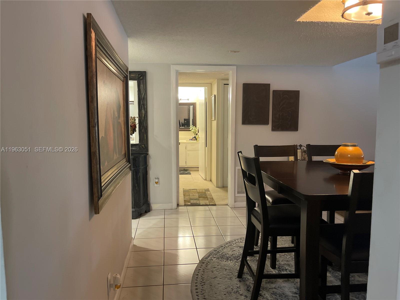 A dining area with a dark wood table leads into a hallway toward a bathroom — 16475 Golf Club Rd # 309, Weston FL 33326, WESTON, FL