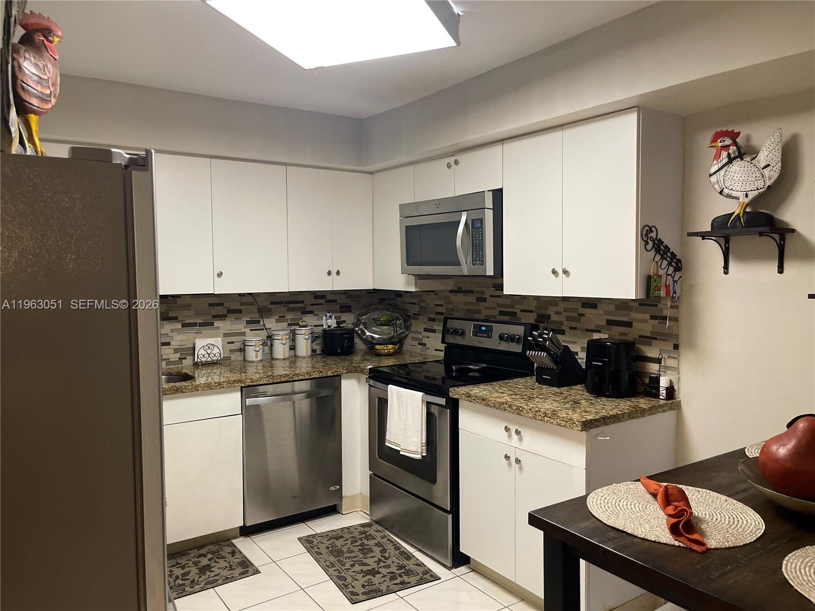 A kitchen features white cabinets, stainless steel appliances, granite countertops, and a tiled backsplash — 16475 Golf Club Rd # 309, Weston FL 33326, WESTON, FL