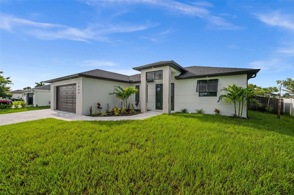 A modern, single-story house with a gray garage, white stucco walls, and a manicured lawn — 1609 NW 16TH TERRACE, CAPE CORAL, FL
