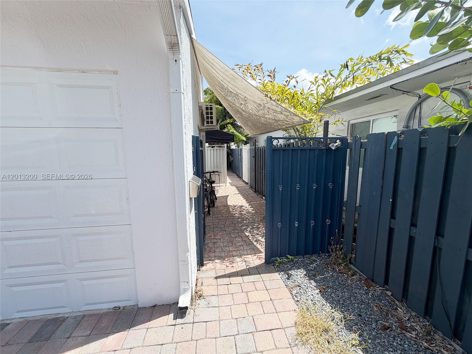 A narrow brick walkway leads between a white garage and a blue fence — 214 NE 108th, Miami FL 33161, MIAMI, FL
