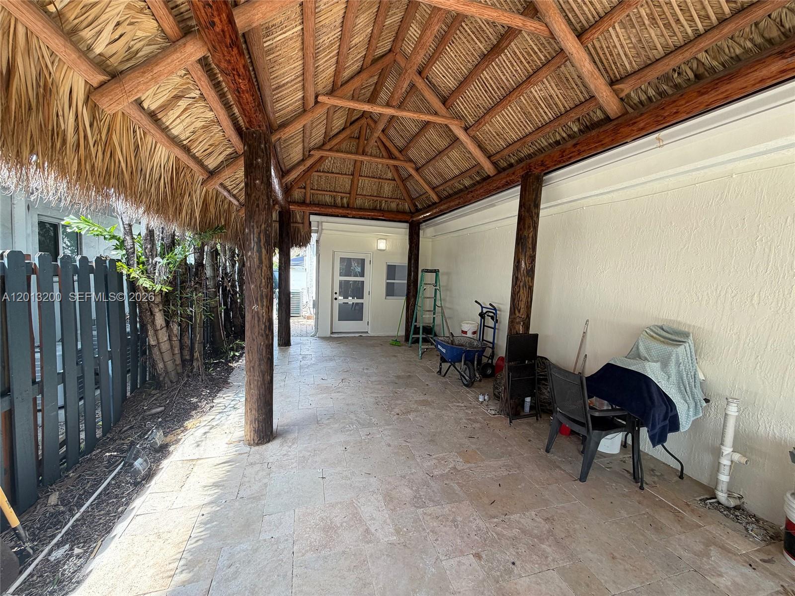 A covered patio features a thatched roof, stone tile flooring, and wooden support columns — 214 NE 108th, Miami FL 33161, MIAMI, FL
