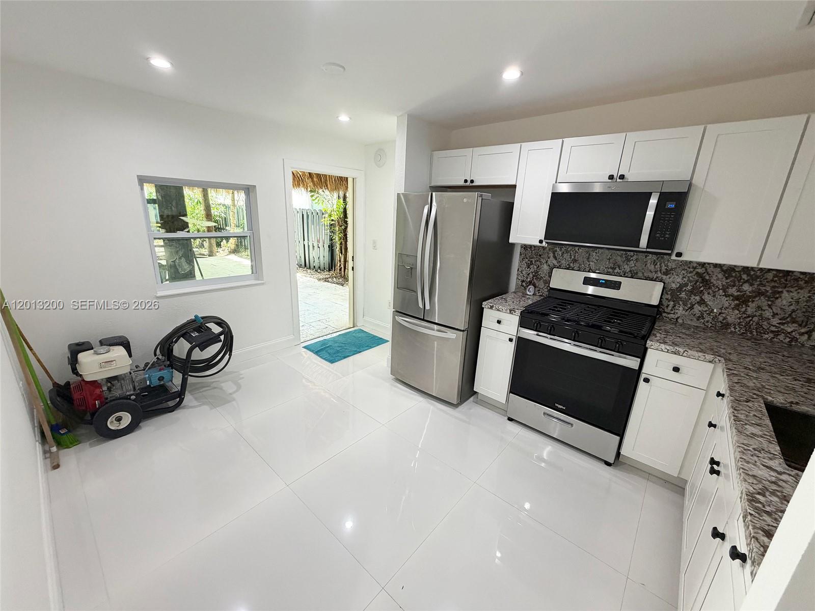 A kitchen with white cabinets, stainless steel appliances, granite countertops, and a pressure washer inside — 214 NE 108th, Miami FL 33161, MIAMI, FL