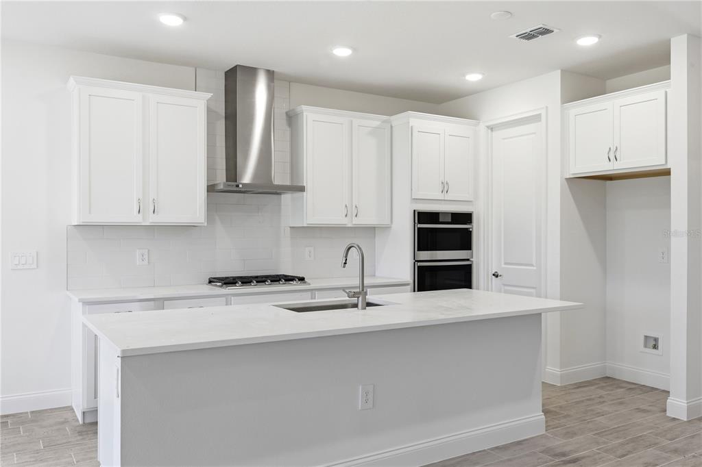 A modern kitchen features white cabinets, stainless steel appliances, a large island, and tile flooring — 2357 WISE RIVER LANE, ZEPHYRHILLS, FL