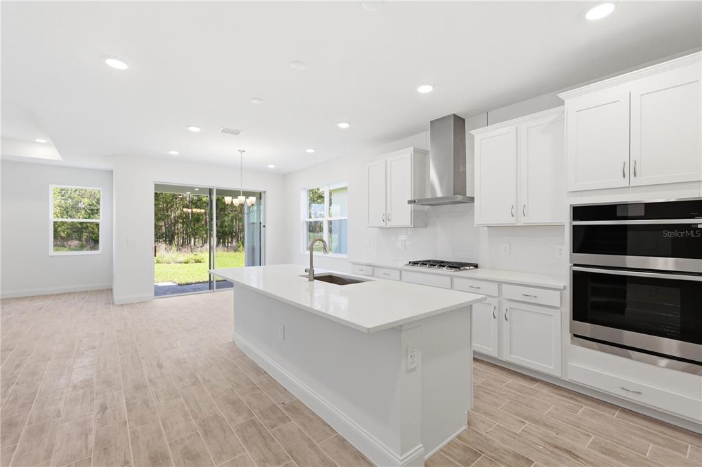 A modern white kitchen features a large island, stainless steel appliances, and wood-look tile flooring — 2357 WISE RIVER LANE, ZEPHYRHILLS, FL