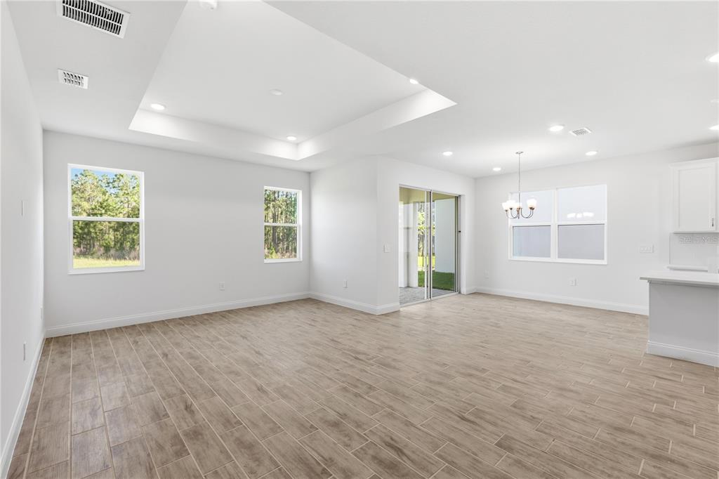 An open-concept living and dining area features white walls, tile flooring, and a tray ceiling — 2357 WISE RIVER LANE, ZEPHYRHILLS, FL