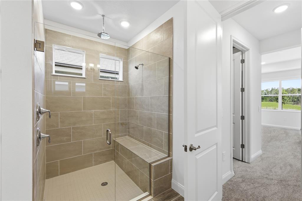 A walk-in shower with beige tile walls, a built-in bench, and glass doors — 2357 WISE RIVER LANE, ZEPHYRHILLS, FL