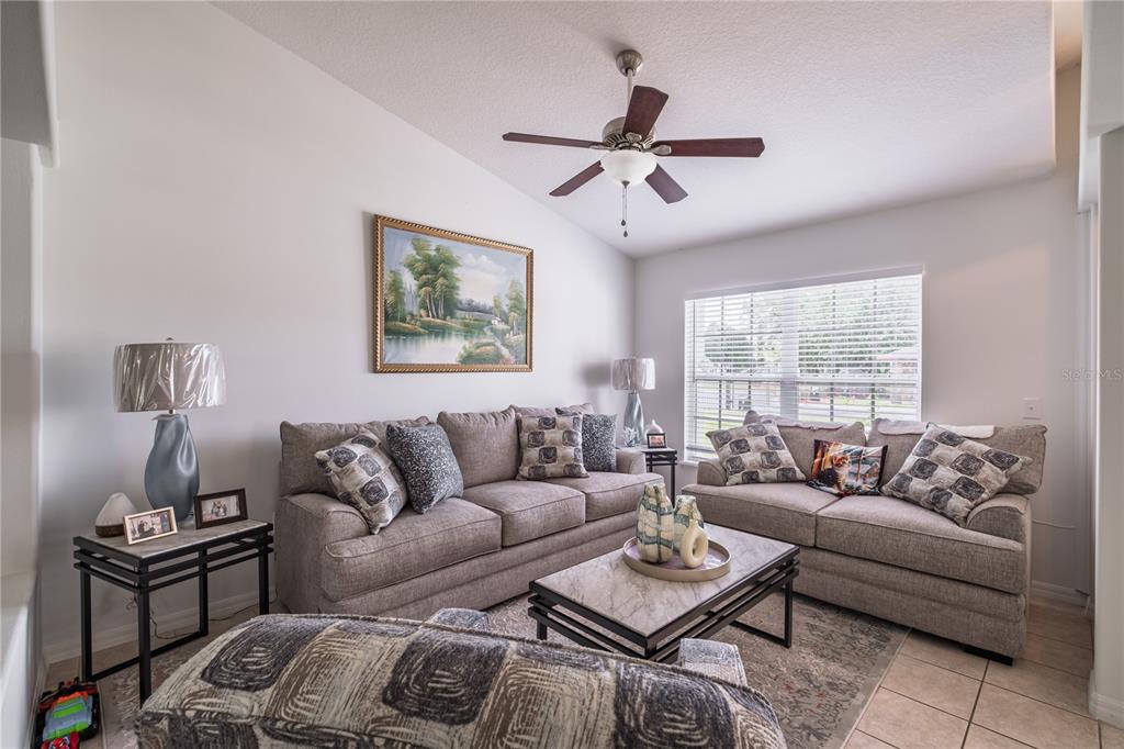 A living room features two gray sofas, a coffee table, and a ceiling fan — 3501 BEAU CHENE DRIVE, KISSIMMEE, FL