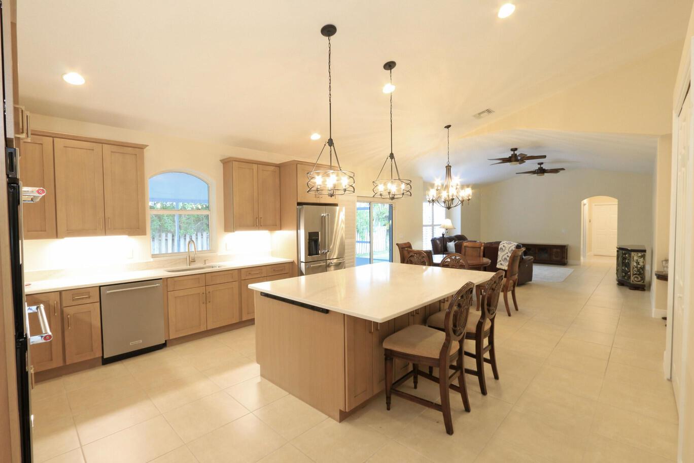 A kitchen features a large light-colored stone island, wood cabinets, and a modern pendant light — 2879 SE Peru Street, FL 34984, FL