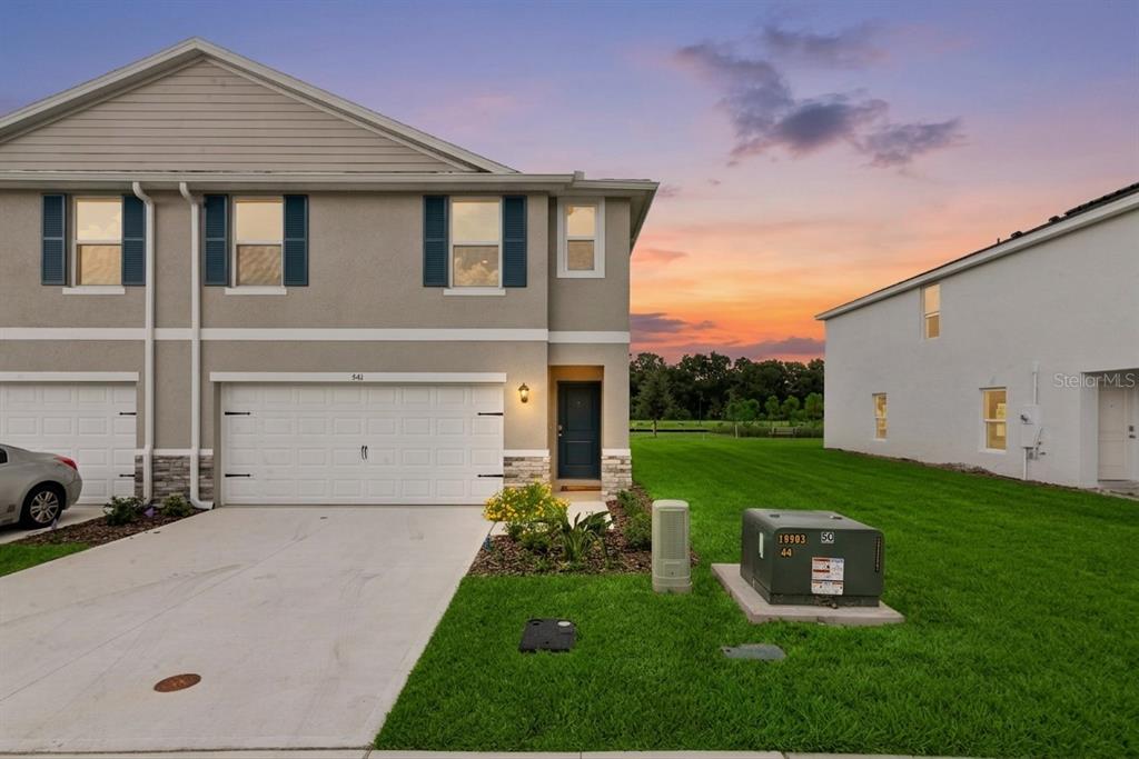 A two-story townhouse exterior with a garage, driveway, and green lawn at sunset — 541 REMICK STREET, OSTEEN, FL