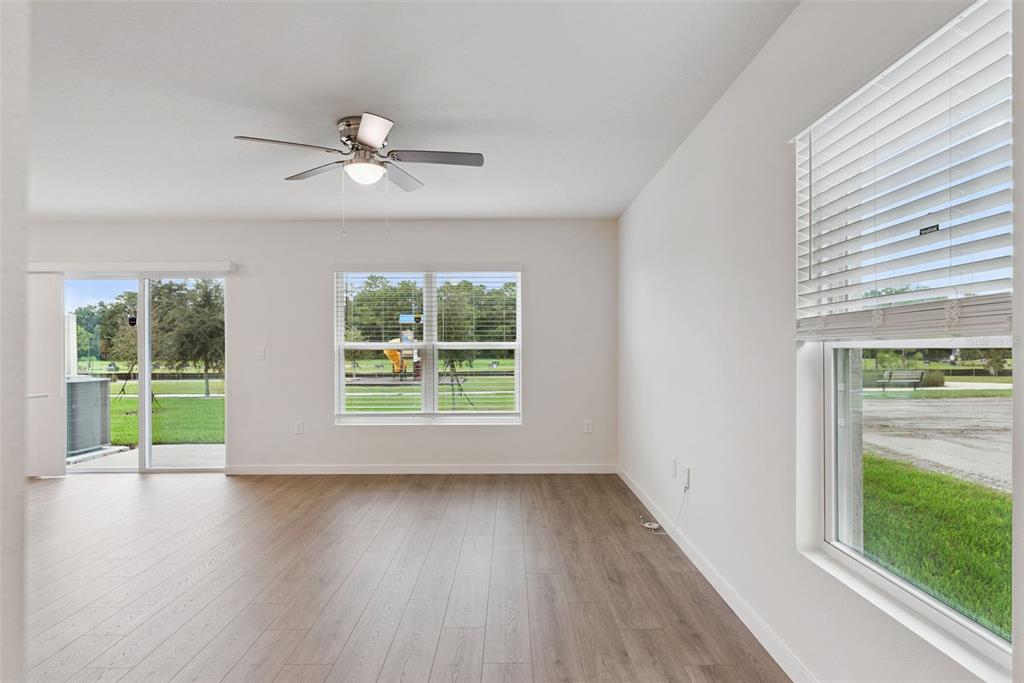 An empty room features light wood-look flooring, a ceiling fan, and windows overlooking a park — 541 REMICK STREET, OSTEEN, FL