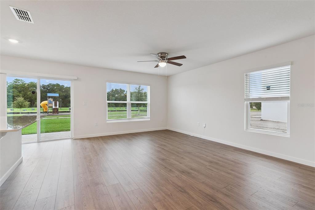 An empty living room features wood-look flooring, a ceiling fan, and sliding glass doors to a yard — 541 REMICK STREET, OSTEEN, FL