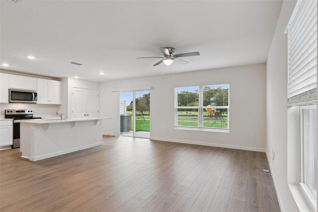 An open-concept kitchen and living area with white cabinets, wood-look flooring, and sliding glass doors — 541 REMICK STREET, OSTEEN, FL