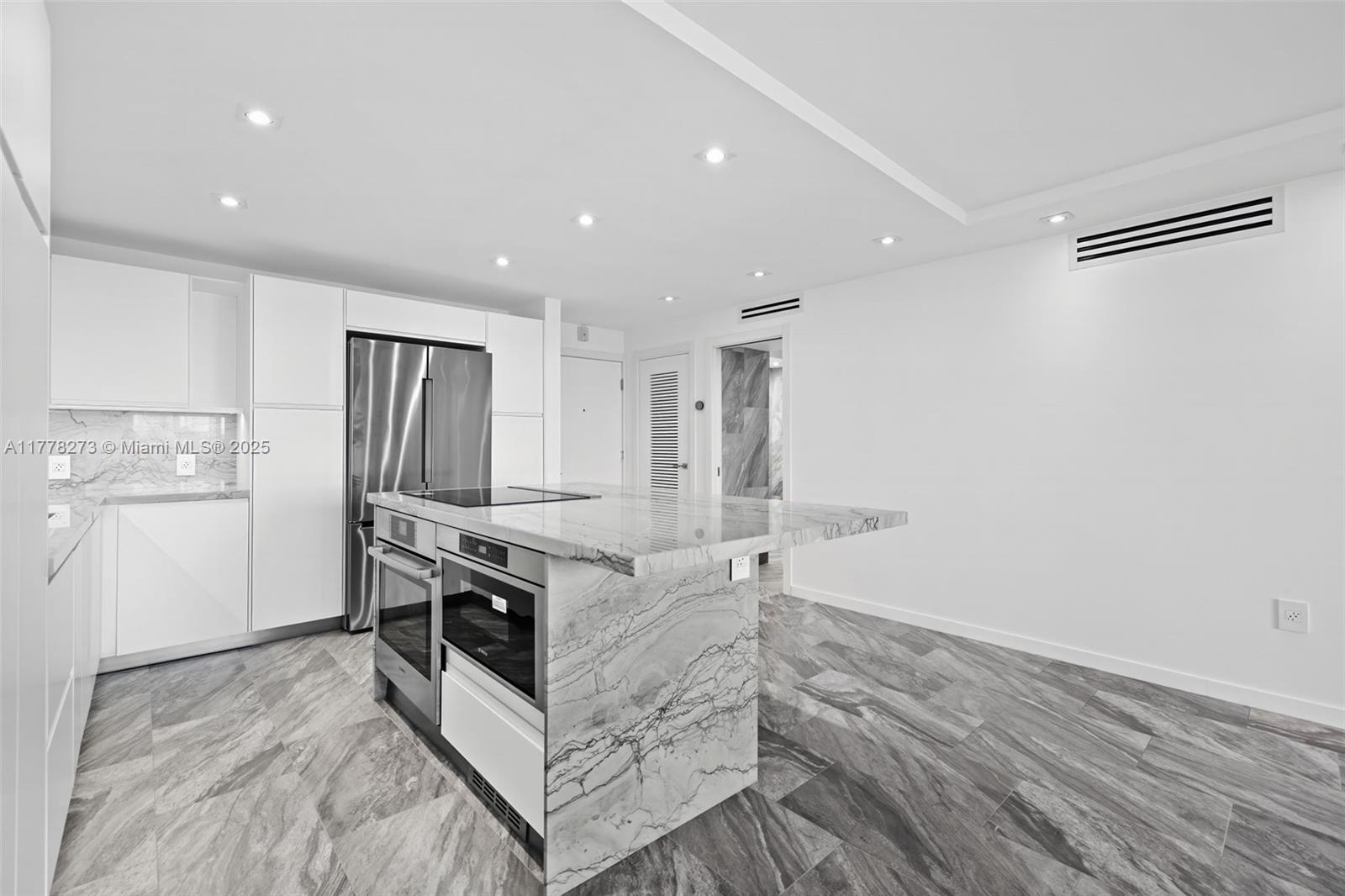 A modern kitchen features white cabinetry, a marble-topped island, and gray patterned tile flooring — 1658 Bay Rd # 504, Miami Beach FL 33139, MIAMI BEACH, FL