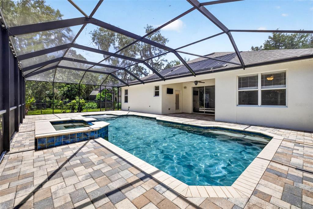 A swimming pool and attached spa are enclosed within a screened lanai behind a house — 6135 WHIMBRELWOOD DRIVE, LITHIA, FL