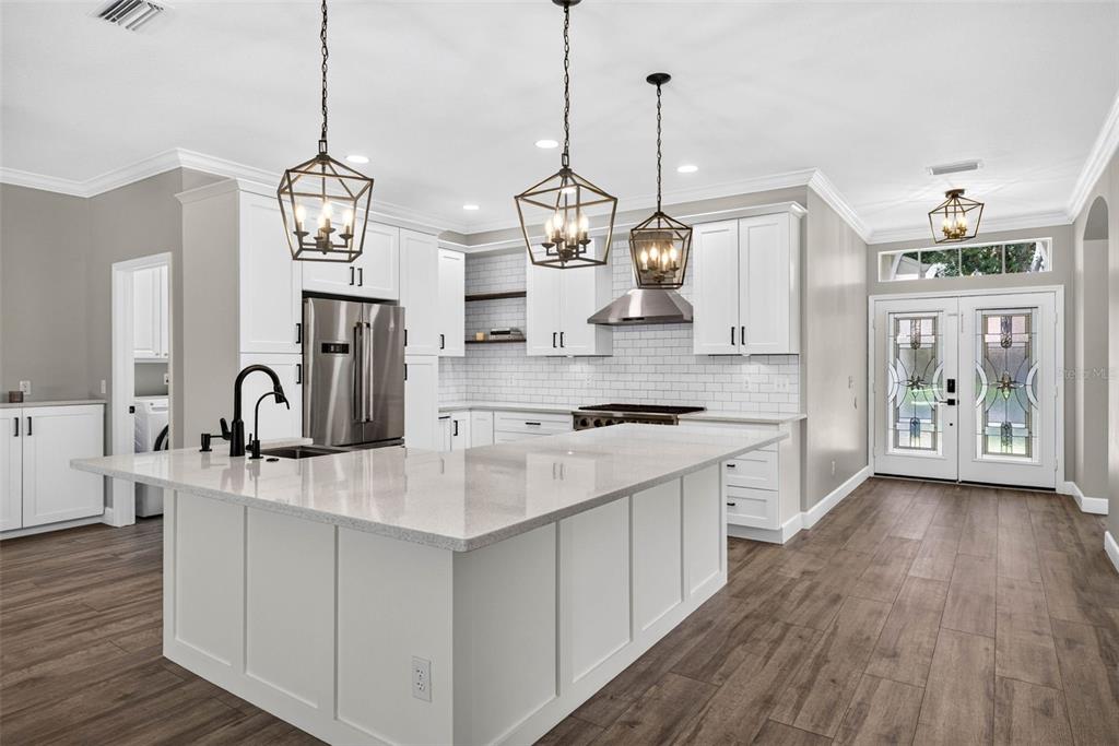A modern kitchen features white cabinets, a large quartz island, and three hanging lantern pendants — 6135 WHIMBRELWOOD DRIVE, LITHIA, FL