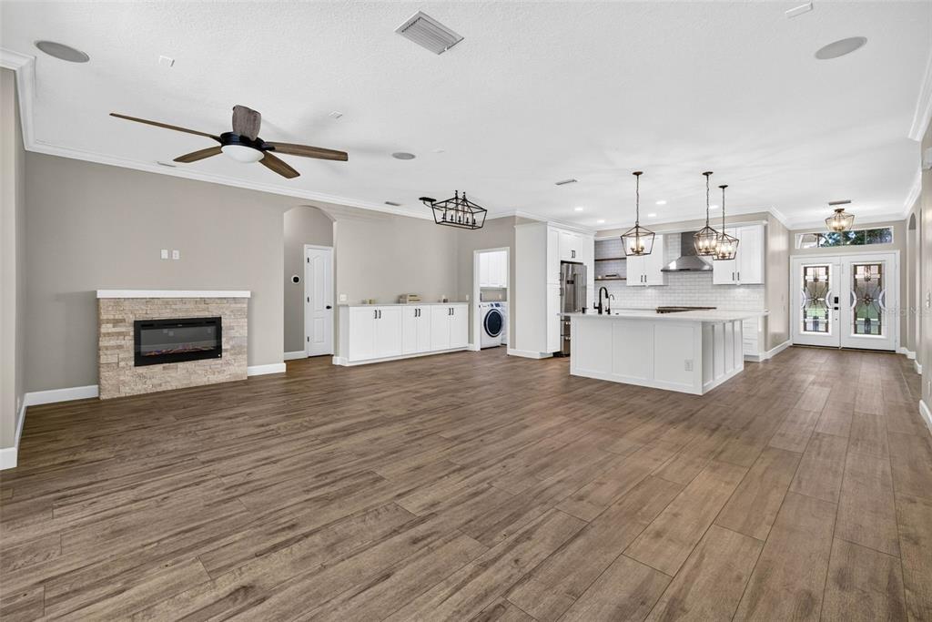 An open-concept living area features a stone fireplace, wood-look flooring, and a white kitchen island — 6135 WHIMBRELWOOD DRIVE, LITHIA, FL