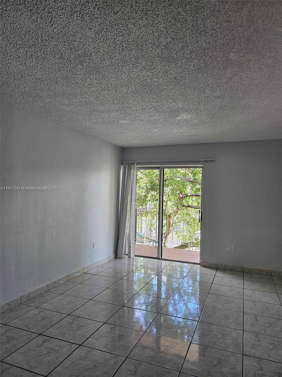 An empty room features light-colored tile flooring, a popcorn ceiling, and a sliding glass door — 8101 SW 73rd Ave # 30, Miami FL 33143, MIAMI, FL