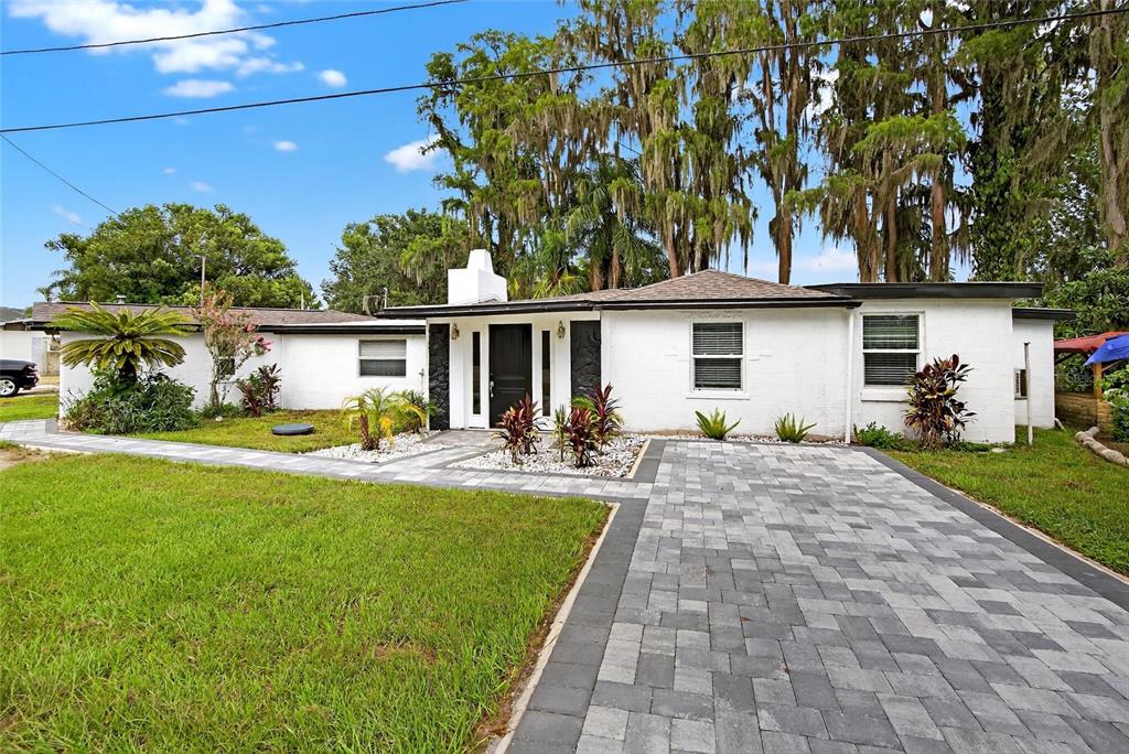 A single-story white house features a paved driveway, walkway, and dark-trimmed front entrance — 5028 SCHOOL ROAD, LAND O LAKES, FL