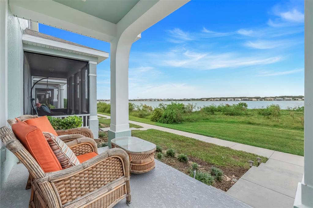 A covered patio with wicker furniture overlooks a grassy lawn and a large lake — 513 JUNIPER SPRINGS DRIVE, GROVELAND, FL